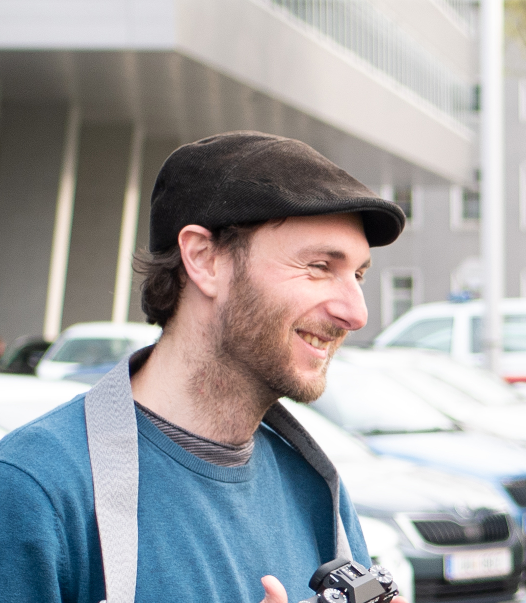Christof Schöffl. Mann Mitte 30. Trägt dunkle Kappe. Nach rechts gewandt. Lächelt.